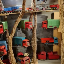 Verzameling speelgoedvrachtwagens in rood en groen uitgestald tegen donkere wand, tussen touwdecoratie
