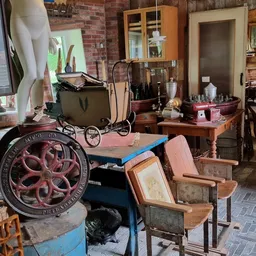 Vintage en tweedehands spullen op de winkelvloer: decoratieve wielen, kinderwagen, houten meubels, frames en diverse attribut