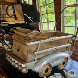 Vintage kinderwagen met beige/bruin canvas en zilveren frame, geëxposeerd in een interieur met grote ramen
