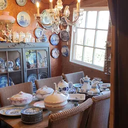 Eetkamer met gedeckte tafel, blauw-witte borden aan de muur, glazen vitrinekast en raam met uitzicht