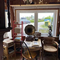 Winkelinterieur met vintage meubels, grammofoon, boekenrekken en grote ramen met uitzicht op parkeerplaats