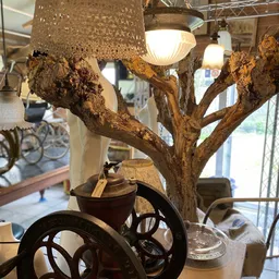 Vintage houten boom-sculptuur met takken, versierd met hanglampen en decoratieve elementen in een winkelinterieur