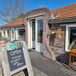Bakstenen gevel van vintage- en boekhandel met terracotta dakpannen, grote ramen en open deur, met OPEN-bord op het terras
