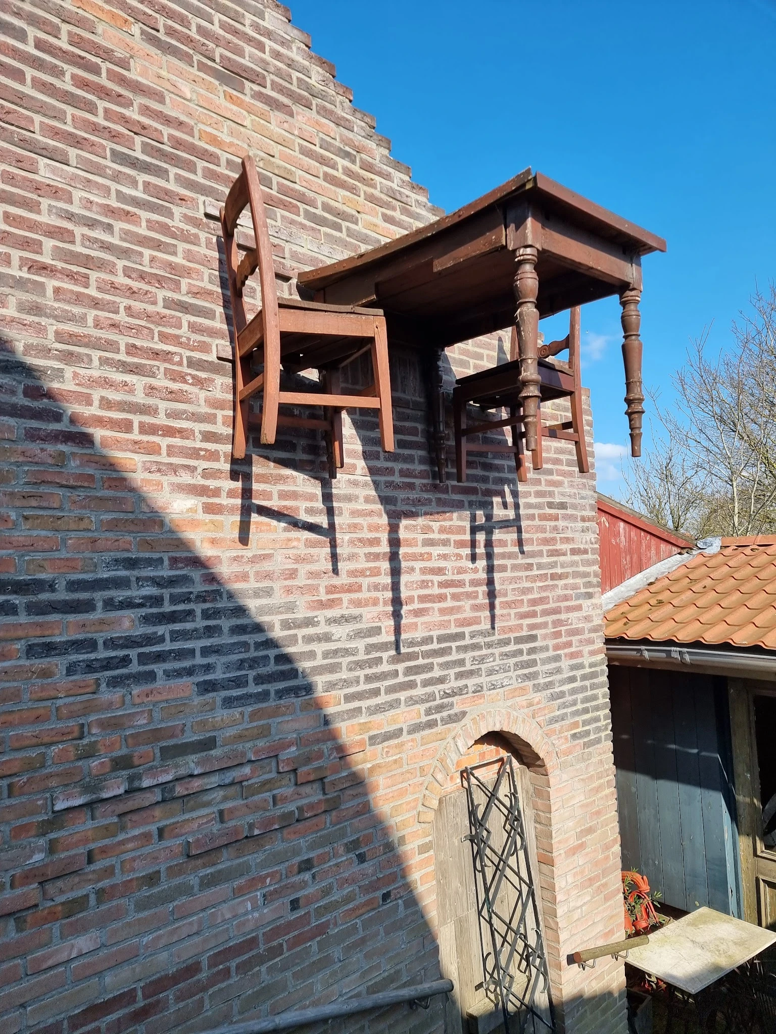 Bakstenen gevel met houten raamkozijn en balkonstructie, gedeeltelijk in schaduw
