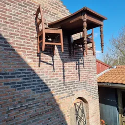 Bakstenen gevel met houten raamkozijn en balkonstructie, gedeeltelijk in schaduw