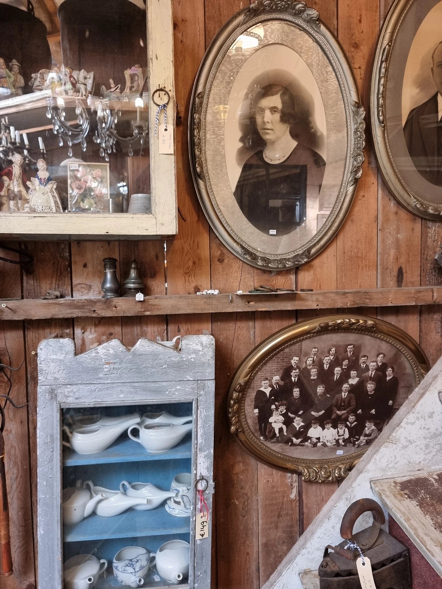 Houten wand met vintage spullen: foto's in lijsten, oude flessen, servies en groepsfoto's