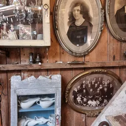 Houten wand met vintage spullen: foto's in lijsten, oude flessen, servies en groepsfoto's