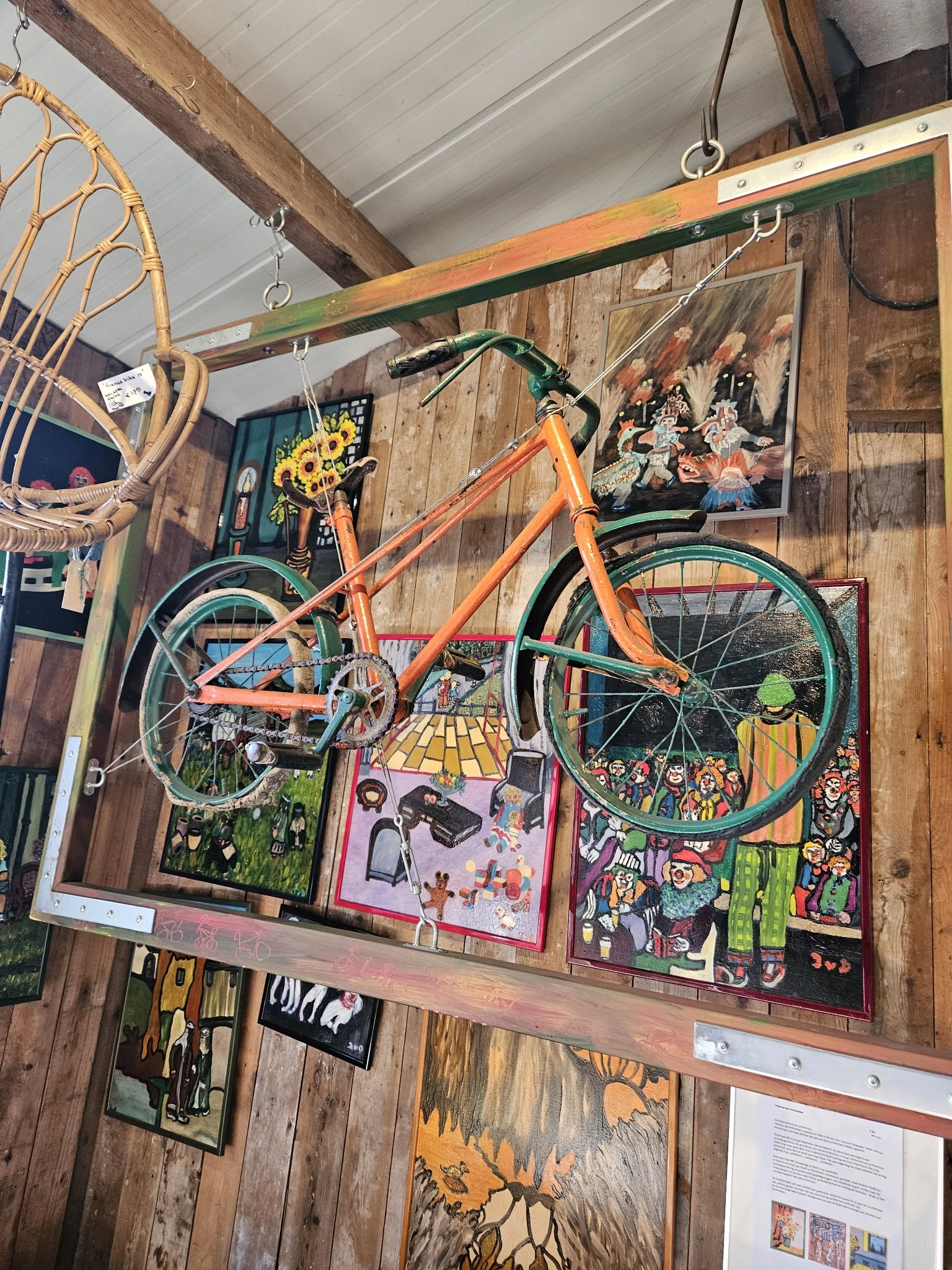 Winkelmuur versierd met vintage items: oranje fiets, houten paneelwand, schilderijen, decoratieve objecten en kunstwerk