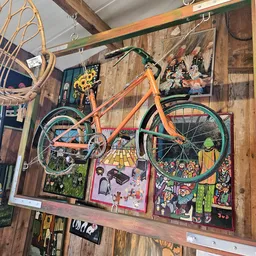 Winkelmuur versierd met vintage items: oranje fiets, houten paneelwand, schilderijen, decoratieve objecten en kunstwerk