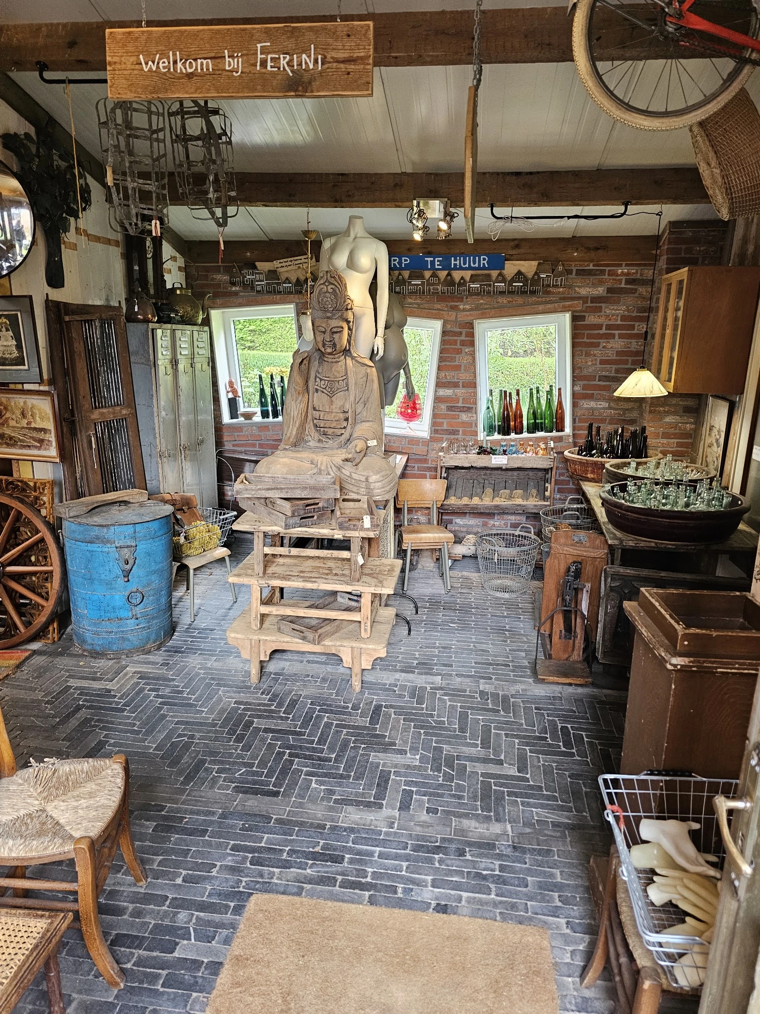 Winkelbinnenkant met boeddhabeeldhouwwerk, vintage meubels, blauwe decoratieve vat en diverse tweedehands artikelen op herrin