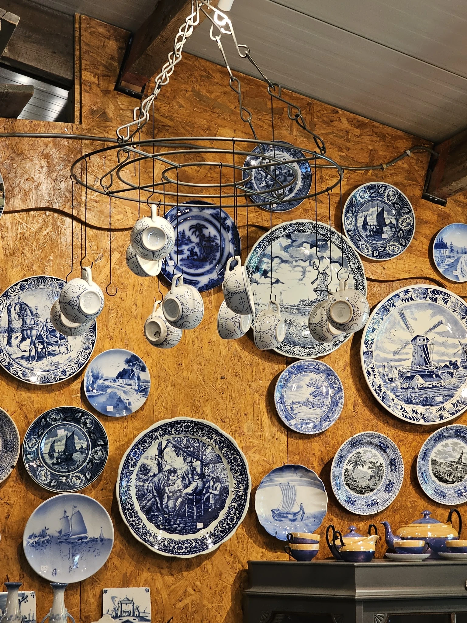 Verzameling vintage blauw-wit servies en porseleinen kopjes aan haakjes tegen houten wand