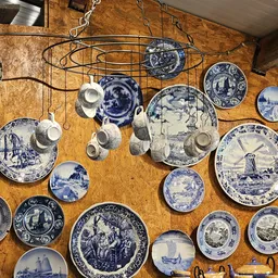 Verzameling vintage blauw-wit servies en porseleinen kopjes aan haakjes tegen houten wand
