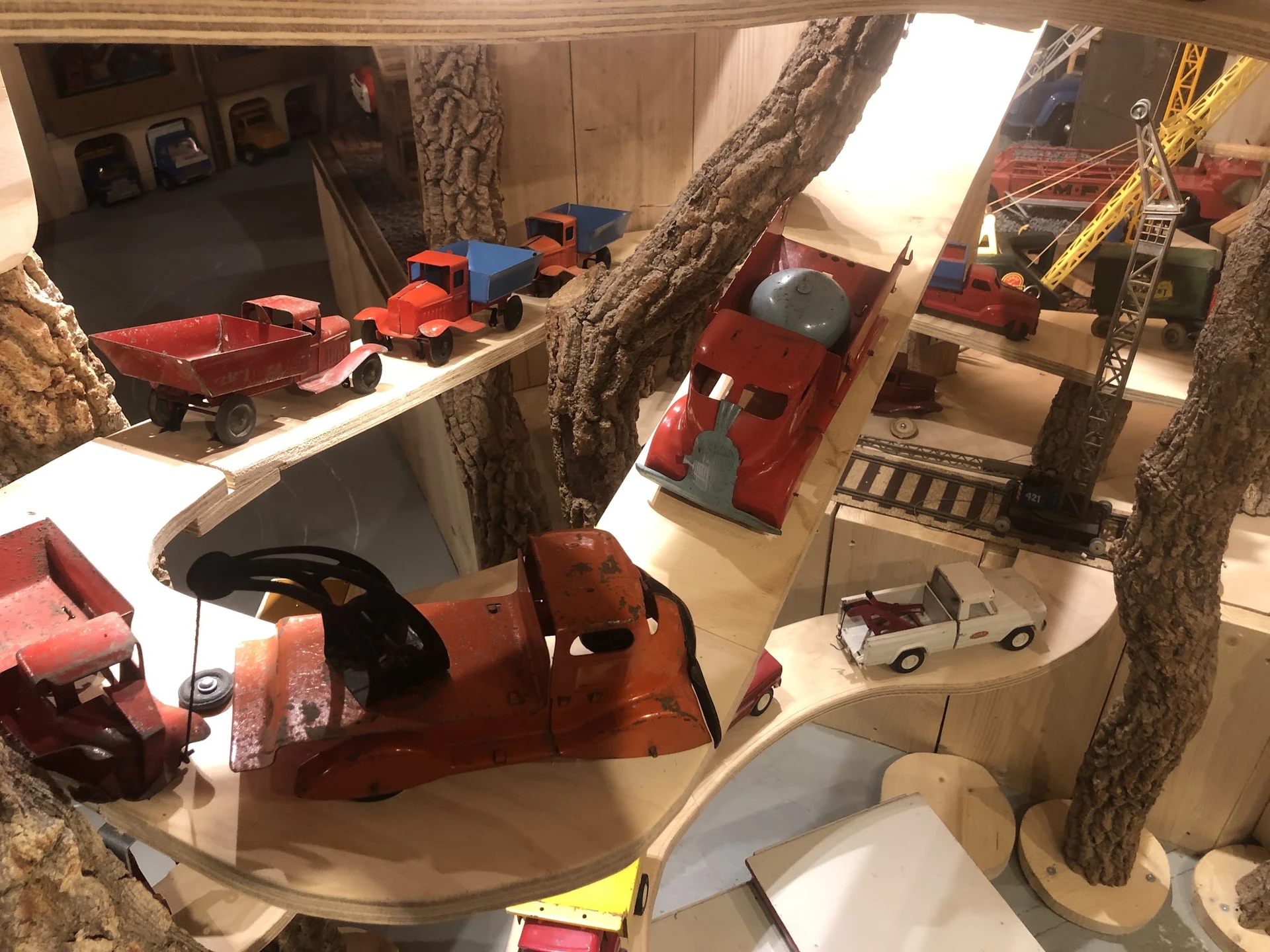Winkelbinnenzicht met grote bomen, speelgoedvoertuigen, modeltreinen en diverse tweedehandsartikelen op display