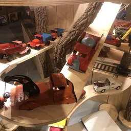 Winkelbinnenzicht met grote bomen, speelgoedvoertuigen, modeltreinen en diverse tweedehandsartikelen op display
