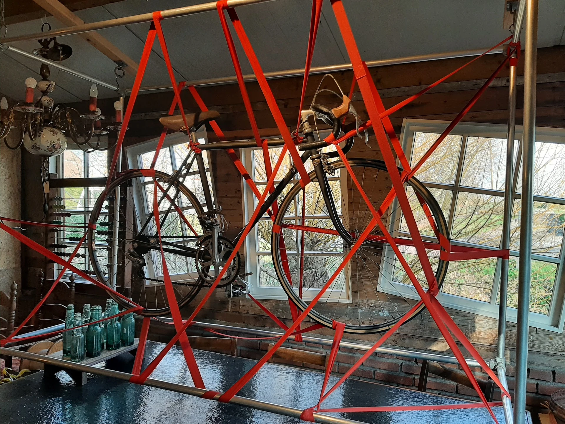 Interieur van winkel met rood stalen frame constructie en fiets opgehangen, grote ramen met uitzicht op straat