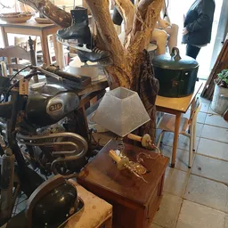 Winkelbinnenruimte met vintage meubels, kunstobjecten, een grote houten boomstronk-sculptuur en diverse tweedehands spullen