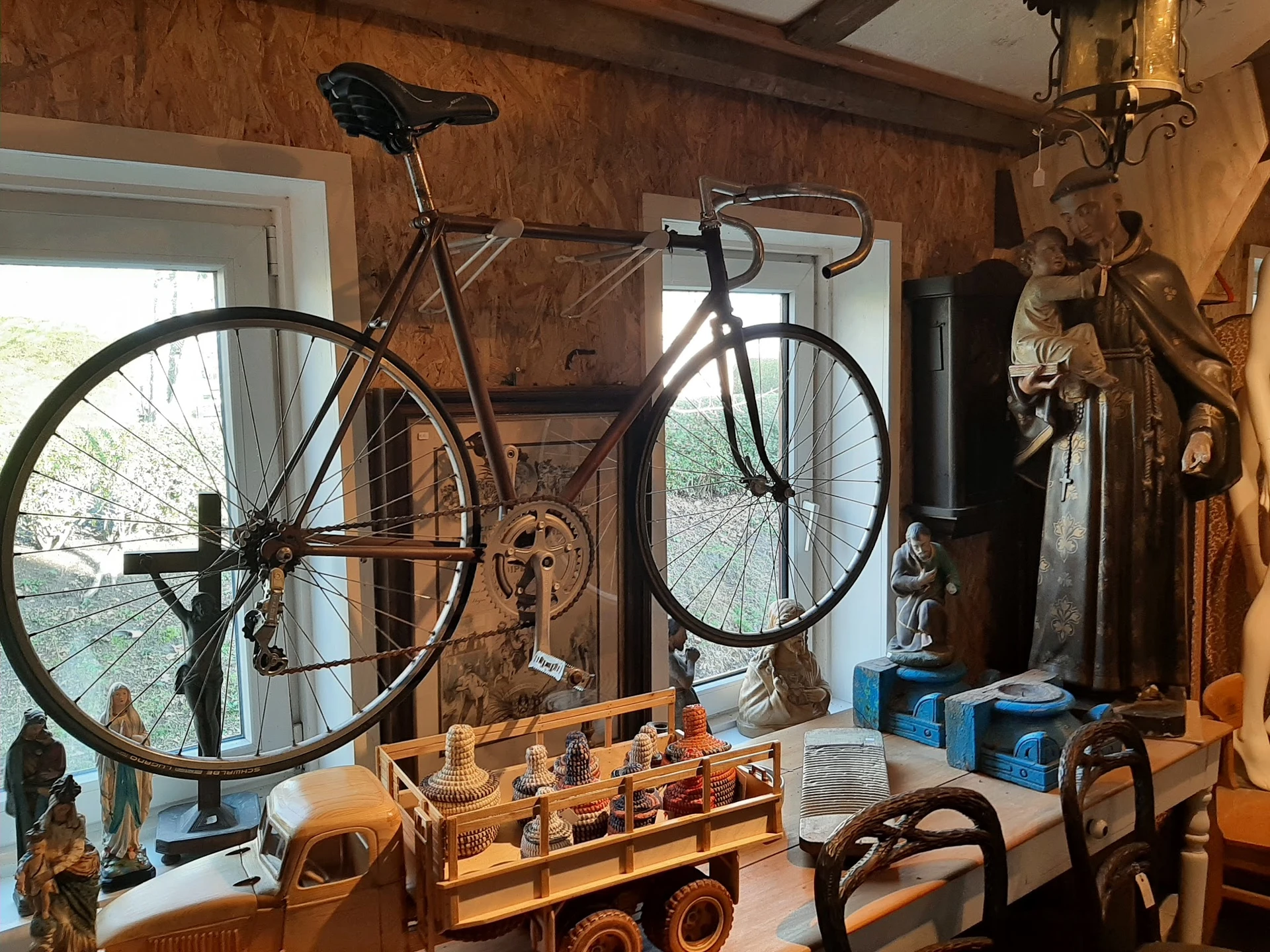 Winkelbinnenruimte met vintage fiets aan muur, houten stellingen met diverse antieke voorwerpen en speelgoed
