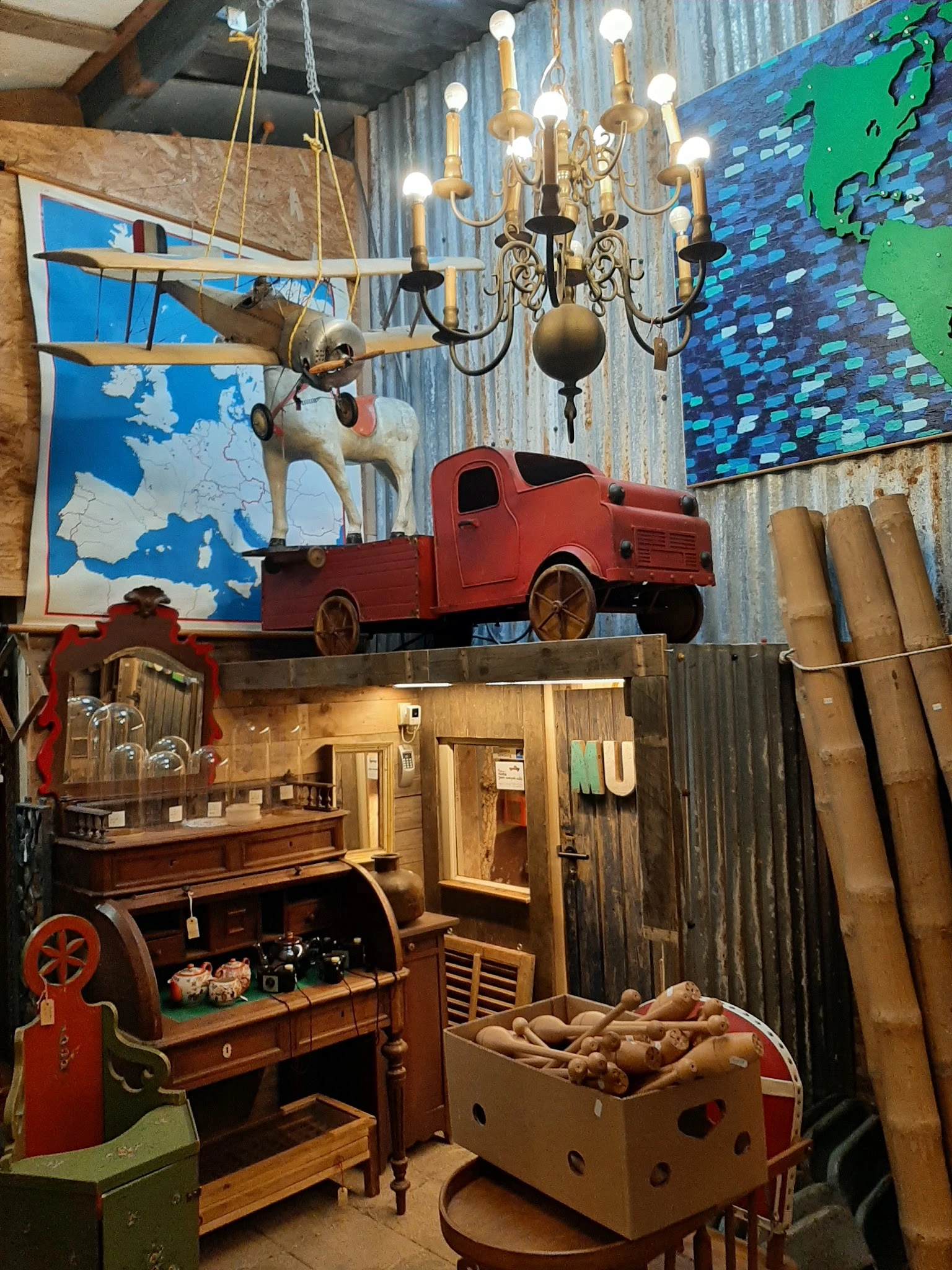 Winkelbinnenkant met vintage decorstukken: rood speelgoedauto, houten huisje, muurkaarten en ophangfiguren