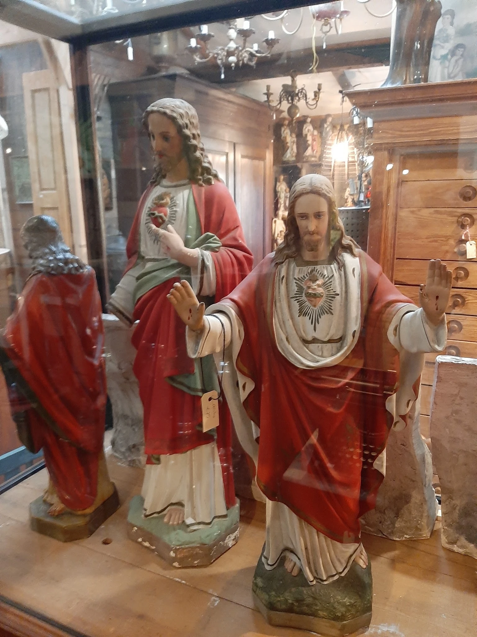 Religieuze beelden en standbeelden in een winkelinterieur, waaronder Jezusfiguren in rode en witte gewaden
