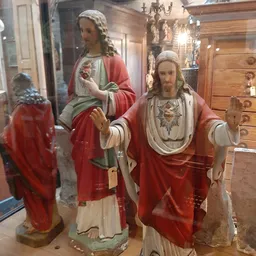 Religieuze beelden en standbeelden in een winkelinterieur, waaronder Jezusfiguren in rode en witte gewaden
