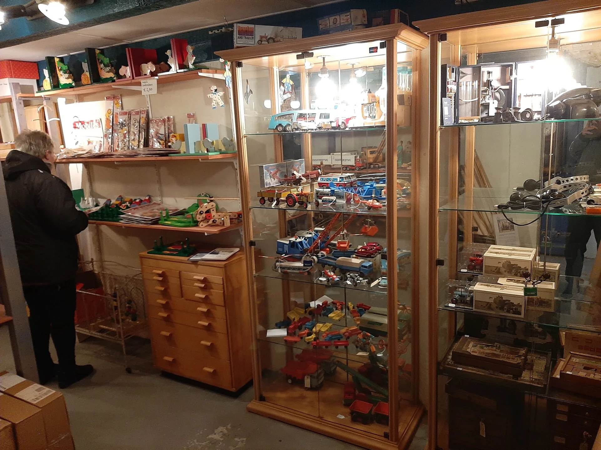 Winkelbinnenruimte met glazen vitrines vol speelgoed en collectibles, houten kasten, stellages en displays met vintage artike