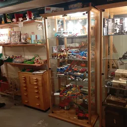 Winkelbinnenruimte met glazen vitrines vol speelgoed en collectibles, houten kasten, stellages en displays met vintage artike
