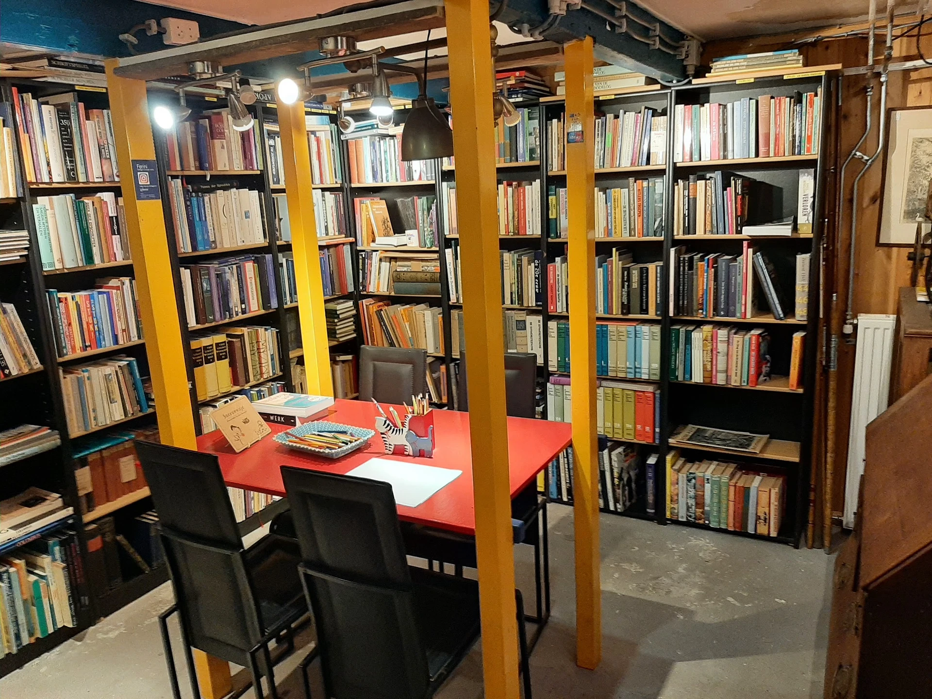 Boekenwinkel interieur met gele zuilen, rode tafel met stoelen en boekenkasten langs de wanden