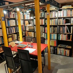 Boekenwinkel interieur met gele zuilen, rode tafel met stoelen en boekenkasten langs de wanden