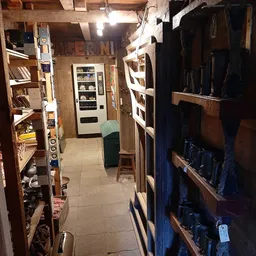 Nauwe winkelgang met boekenkast links, automaat en groen zitje in het midden, en stellingen met artikelen rechts