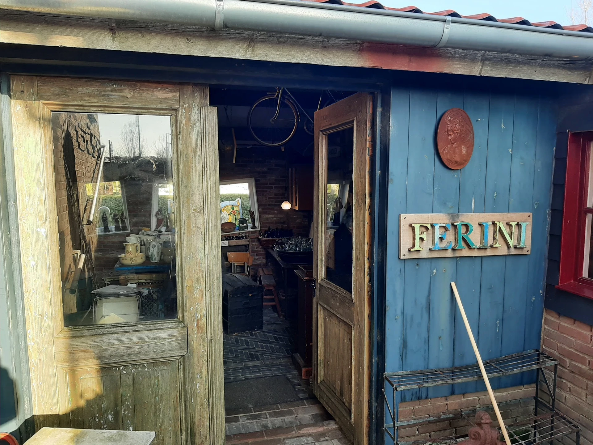 Ingang van vintage winkel Ferini met blauwe gevel, houten deuren en naam op bord