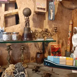 Vintage verzamelobjecten op groene glazen plank: bronzen beeld met basketbal, kandelaar, керамics, boeken en decoratieven.