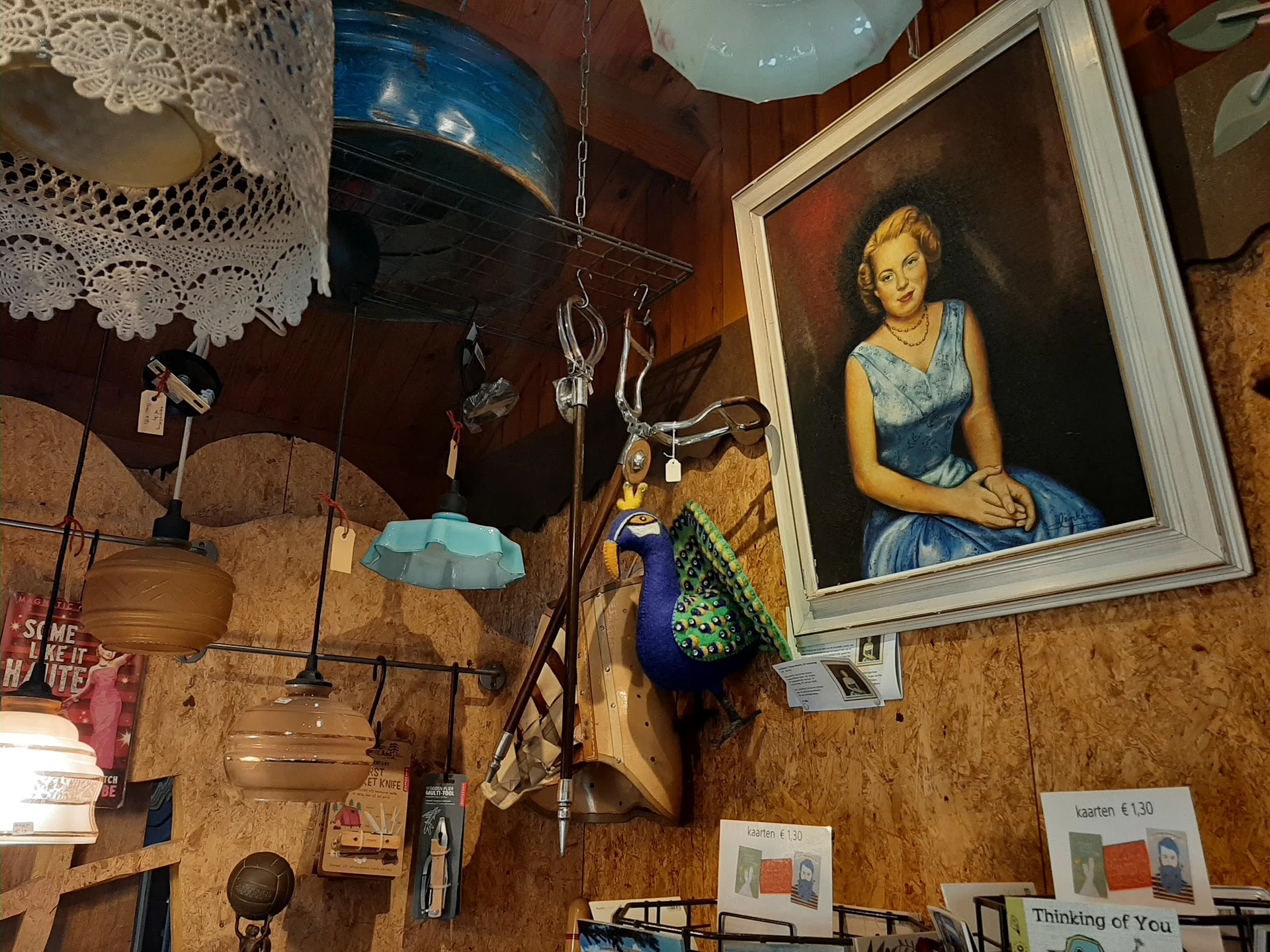 Vintage winkelvloer vol met decoratieve items: portretschilderij aan muur, hangend servies, leren koffers, boeken en diverse 