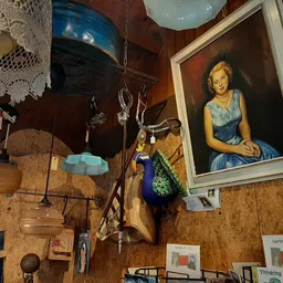Vintage winkelvloer vol met decoratieve items: portretschilderij aan muur, hangend servies, leren koffers, boeken en diverse 