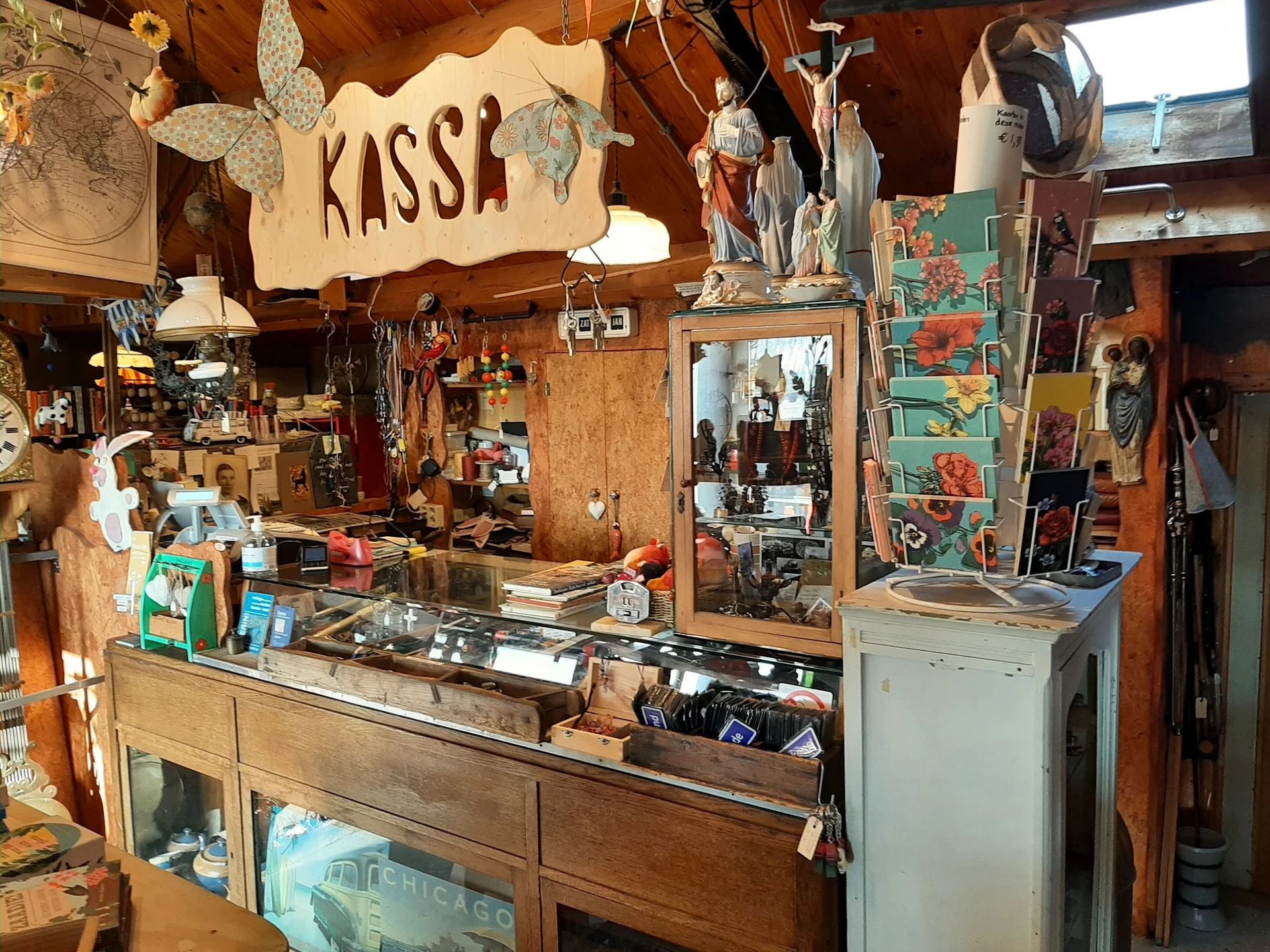 Binnenzicht van vintage tweedehandswinkel met houten toonbank, kassaapparaat en diverse spullen aan muren en plafond