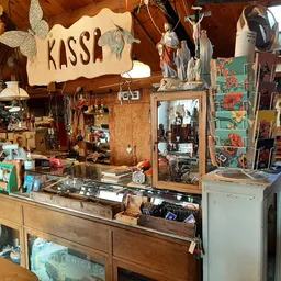 Binnenzicht van vintage tweedehandswinkel met houten toonbank, kassaapparaat en diverse spullen aan muren en plafond