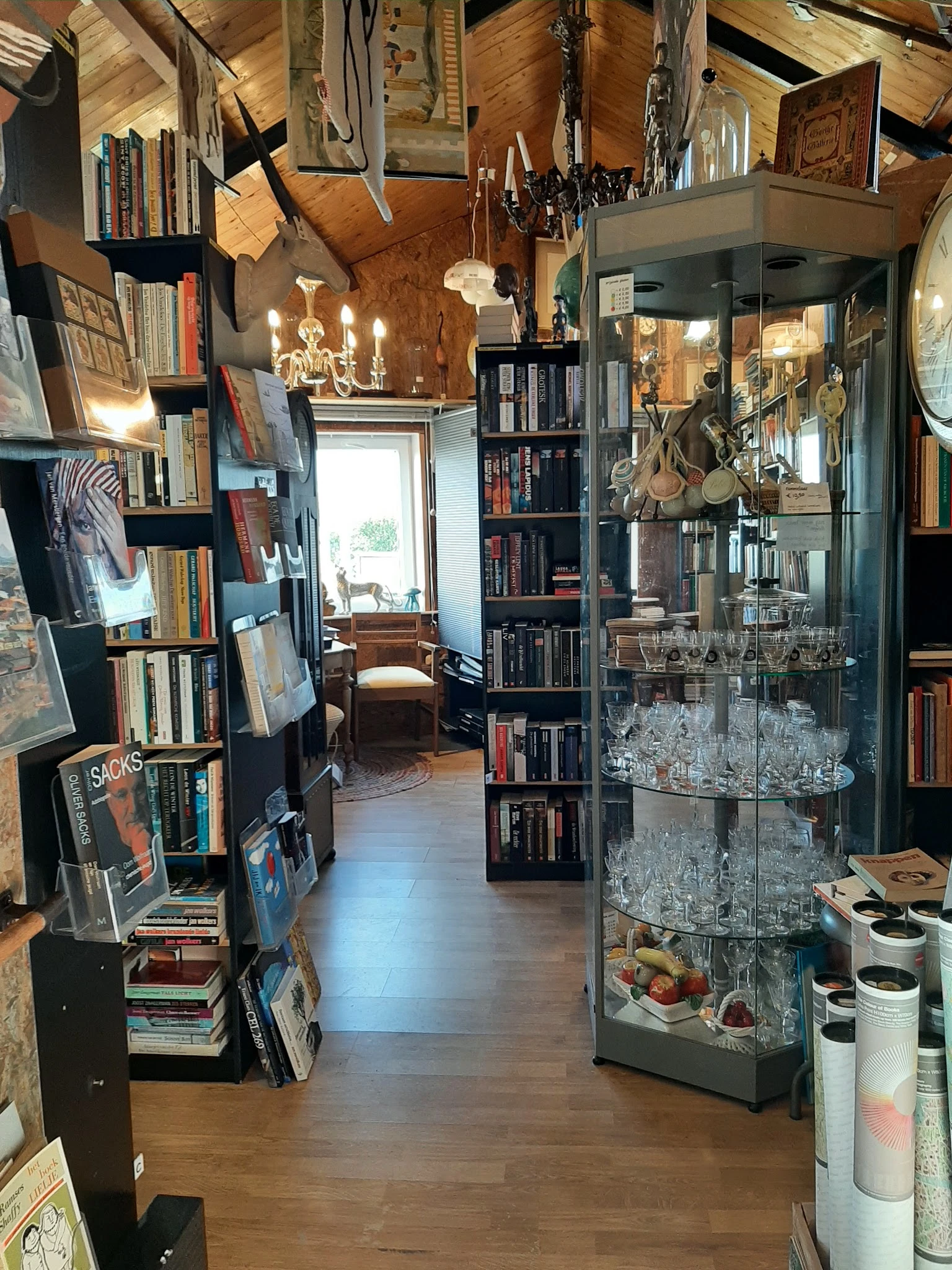 Winkelinterieur met boekenkasten, glazen displaykast met kristalglas, vintage decoratie en boeken langs de wanden