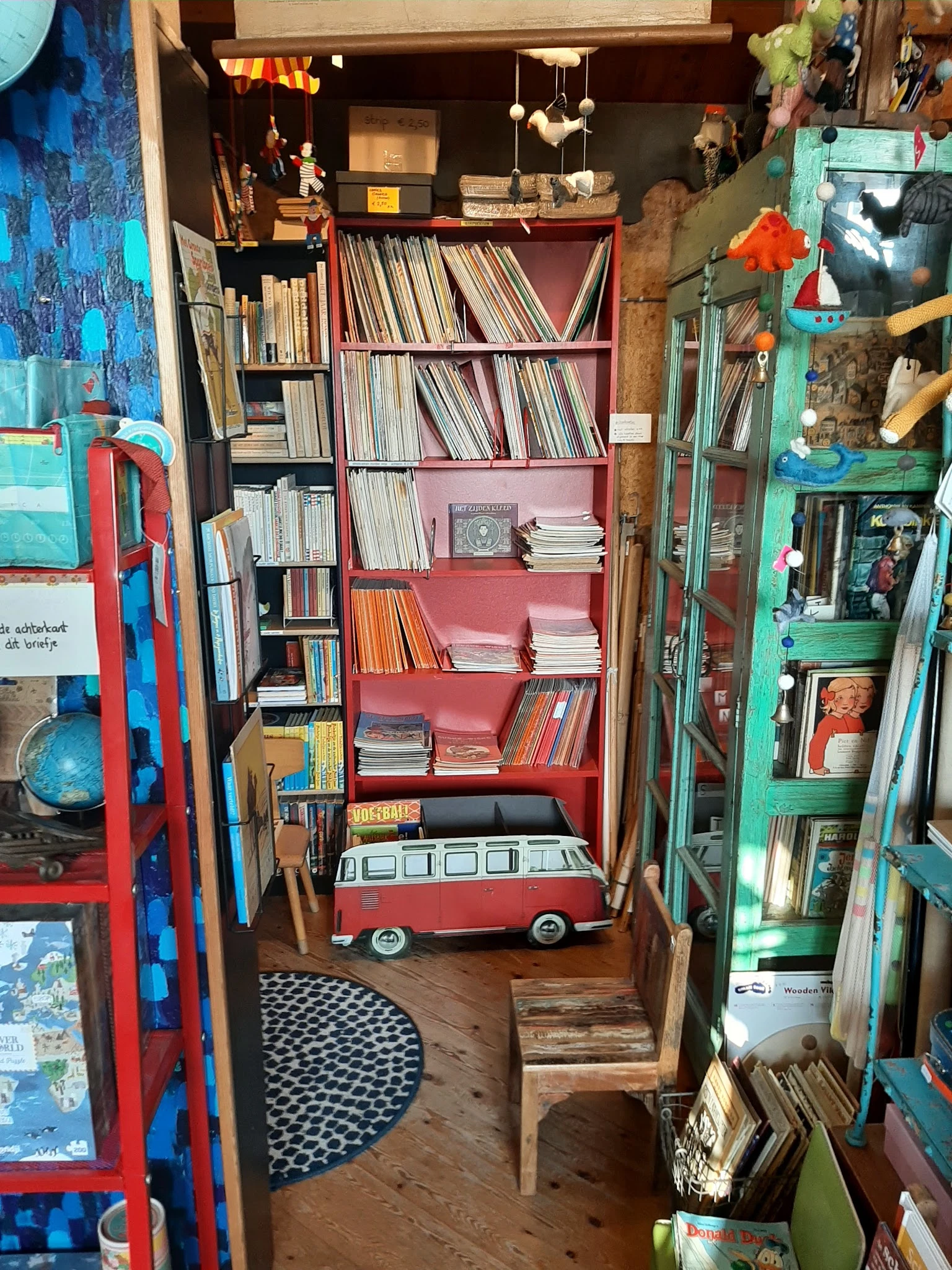 Winkelbinnenkant met boekenkasten, rode en groene stellingen vol met boeken, en decoratiestukken zoals een vintage busmodel