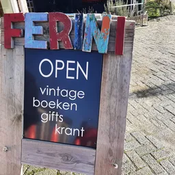 Houten bord met gekleurde letters 'FERINI' en zwart informatiebord met 'OPEN' en winkelomschrijving op straathoek
