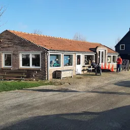 Voorkant van een vintage tweedehands winkel met houten gevel, oranje dak en meerdere ramen, met bezoekers op het voorplein