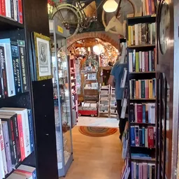 Lange, smalle winkelgang met boekenrekken aan beide zijden, vintage decoraties en een boog boven de deur