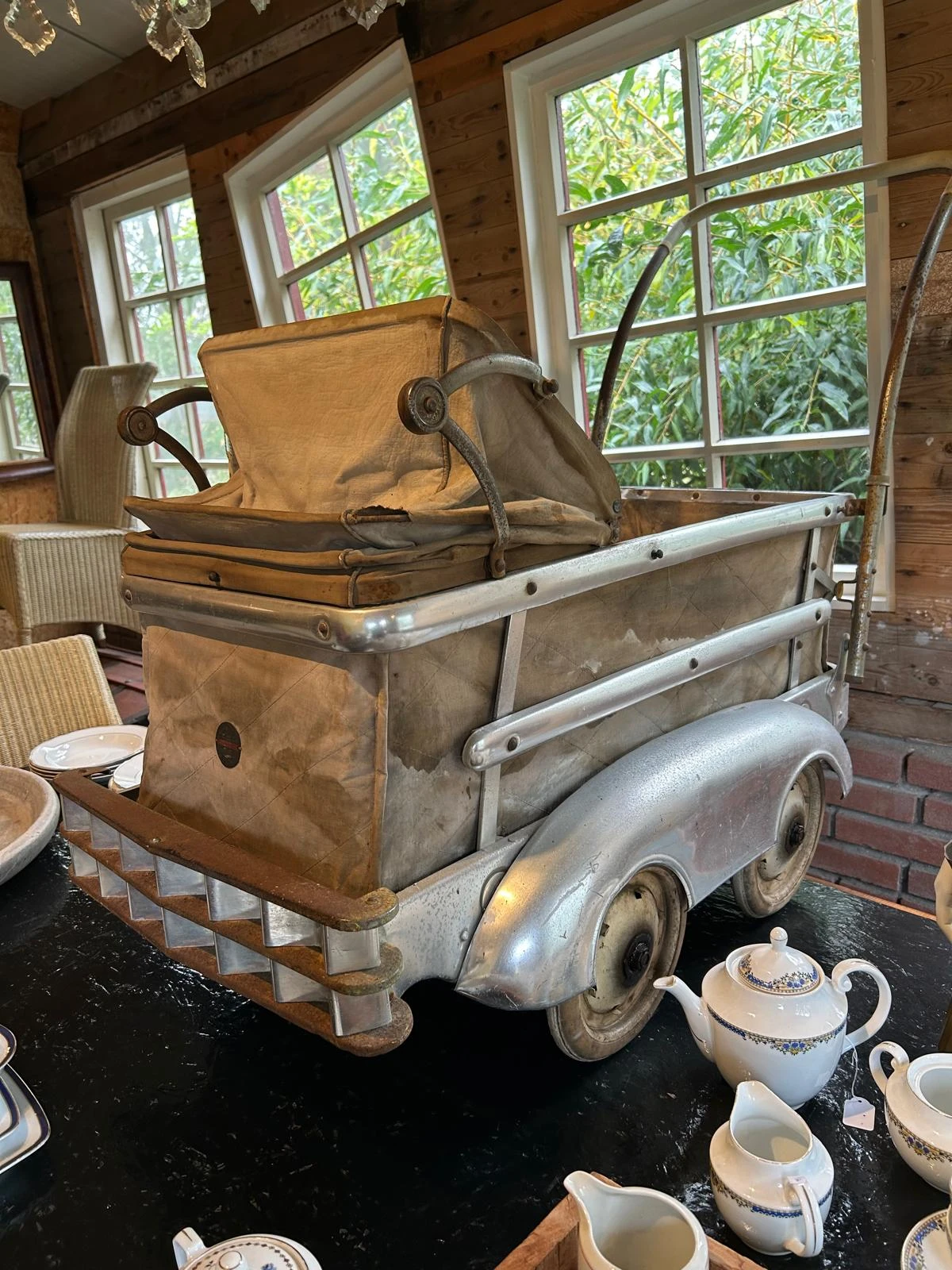 Vintage kinderwagen en speelgoedwagen uitgestald in een interieur met ramen op de achtergrond