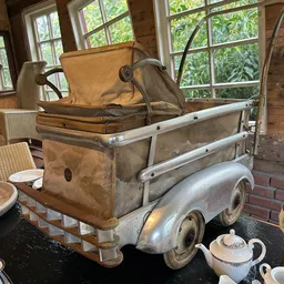 Vintage kinderwagen en speelgoedwagen uitgestald in een interieur met ramen op de achtergrond