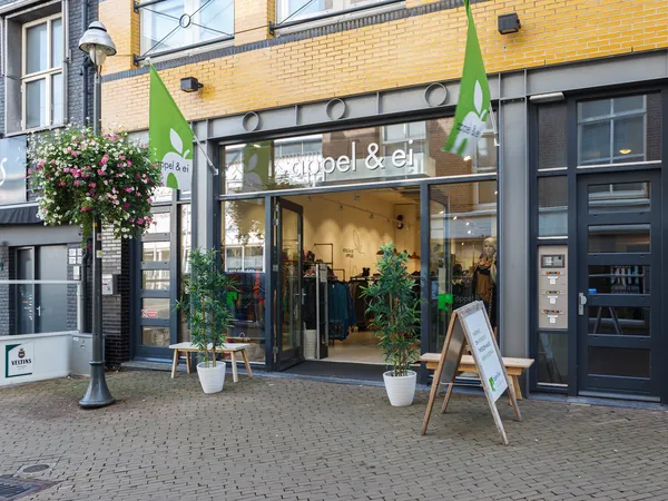 Winkelgevel met groene luifels, glazen deur, uitstallingen en potplanten op het trottoir