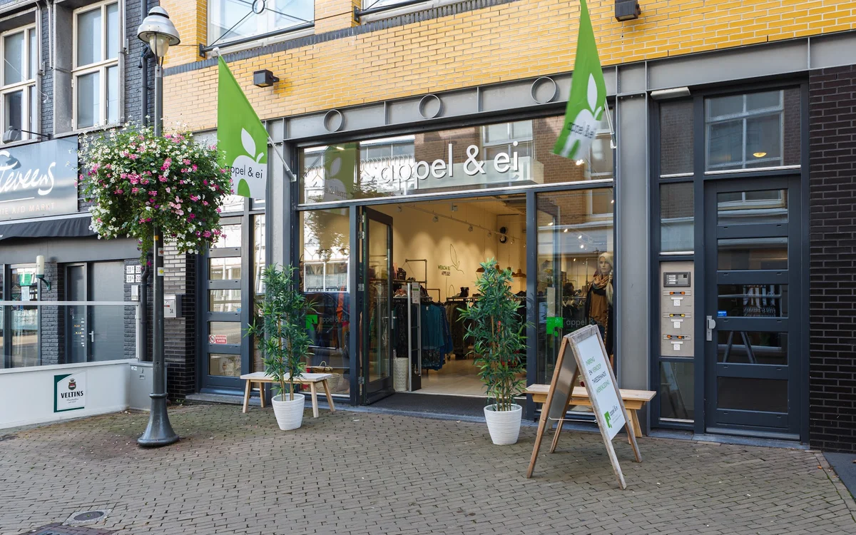 Winkelgevel met groene luifels, glazen deur, uitstallingen en potplanten op het trottoir