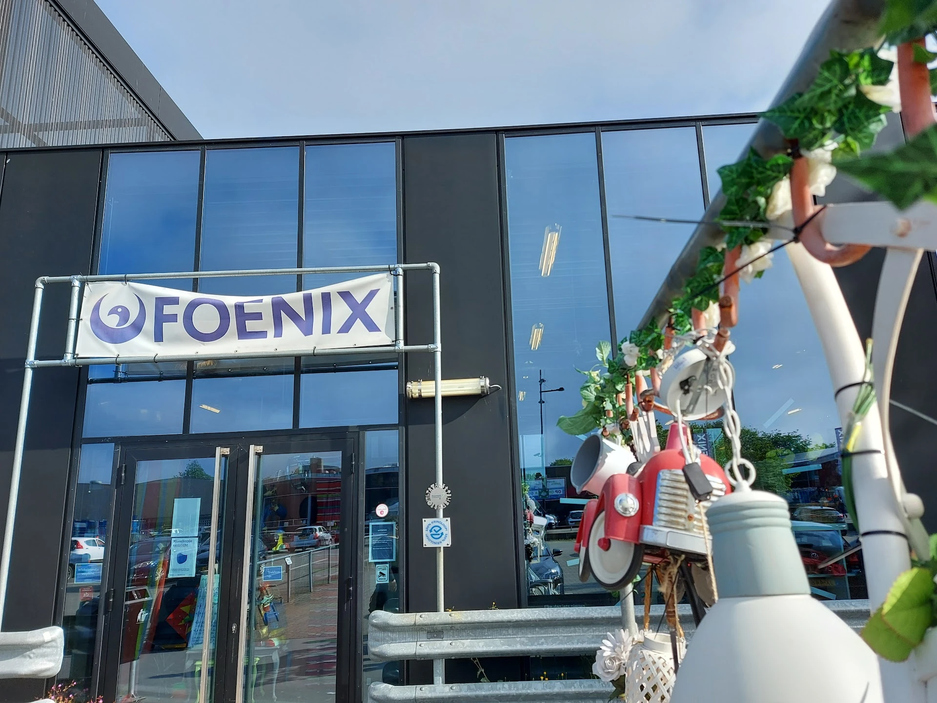 Voorgevel van Foenix kringloopwinkel met grote glazen pui en wit logo, decoratieve fietsen aan de gevel