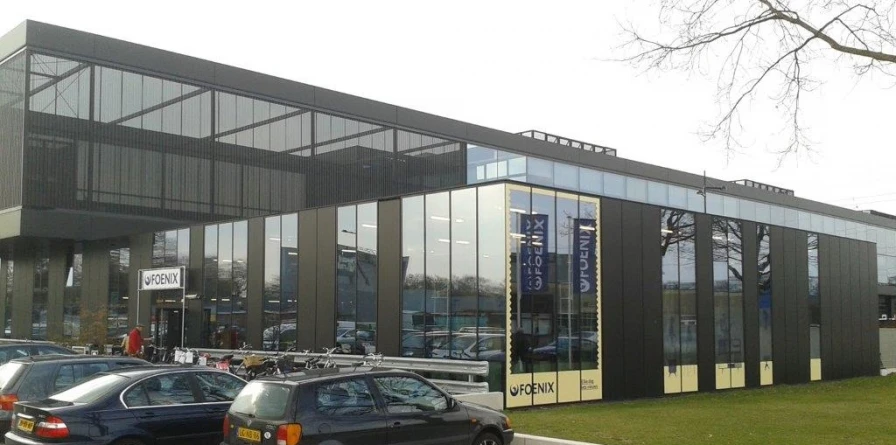 Moderne gevel van kringloopwinkel met grote ramen, zwarte en witte gevelbekleding, en naam Foenix zichtbaar op gele deurinzet