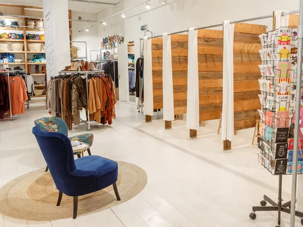 Winkelvloer met kledingrekken, houten scheidingswanden, blauwe stoel op rond tapijt en displaykasten met merchandise