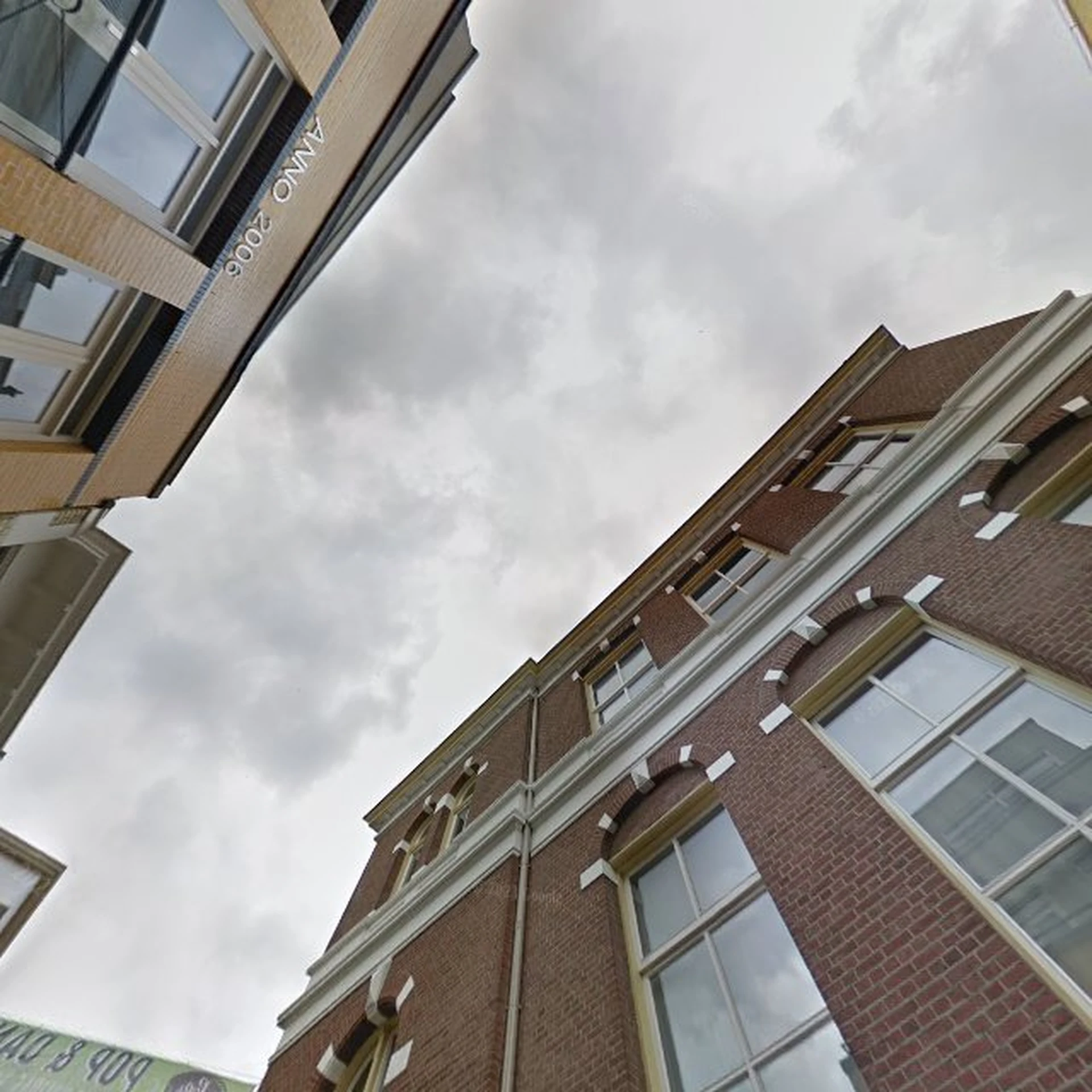 Bovenkant van een bakstenen woongebouw met ramen en dakrand tegen bewolkte lucht.