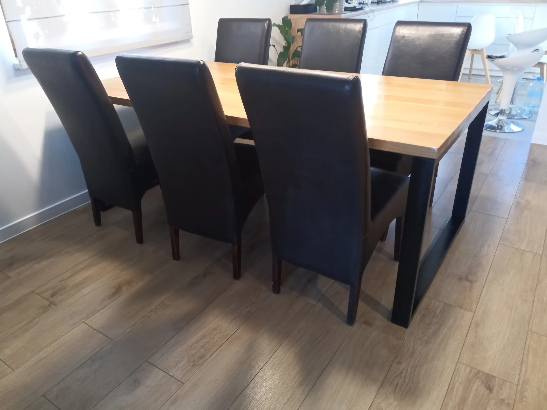 Eettafel met natuurhouten blad en zwarte onderstel, omgeven door zwarte stoelen