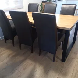 Eettafel met natuurhouten blad en zwarte onderstel, omgeven door zwarte stoelen